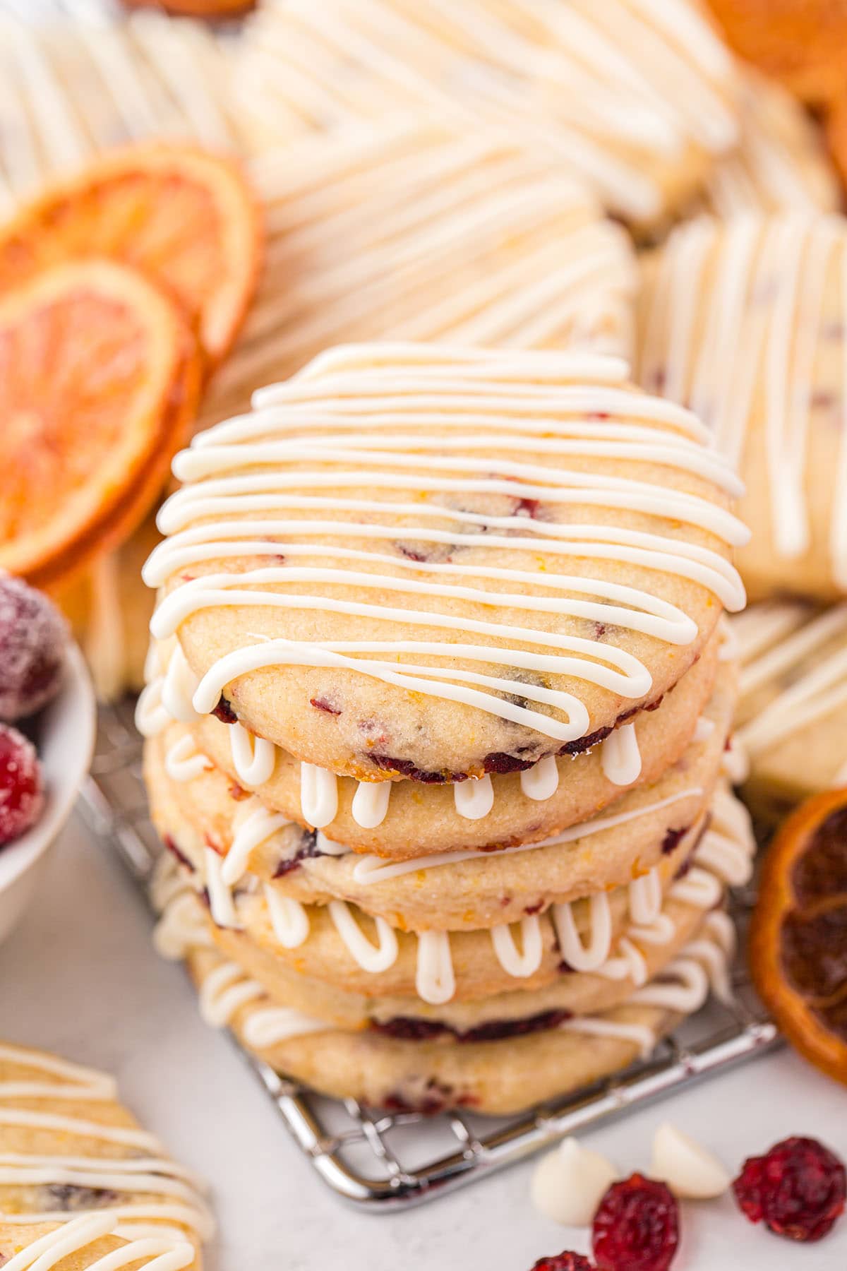Cranberry Orange Shortbread Cookies with white chocolate drizzle stacked on top of cooling rack. 