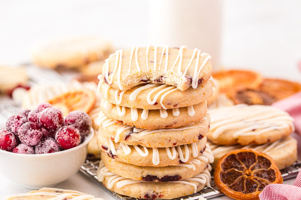 stacked cranberry orange shortbread cookies with dried orange and fresh cranberries on the side. 