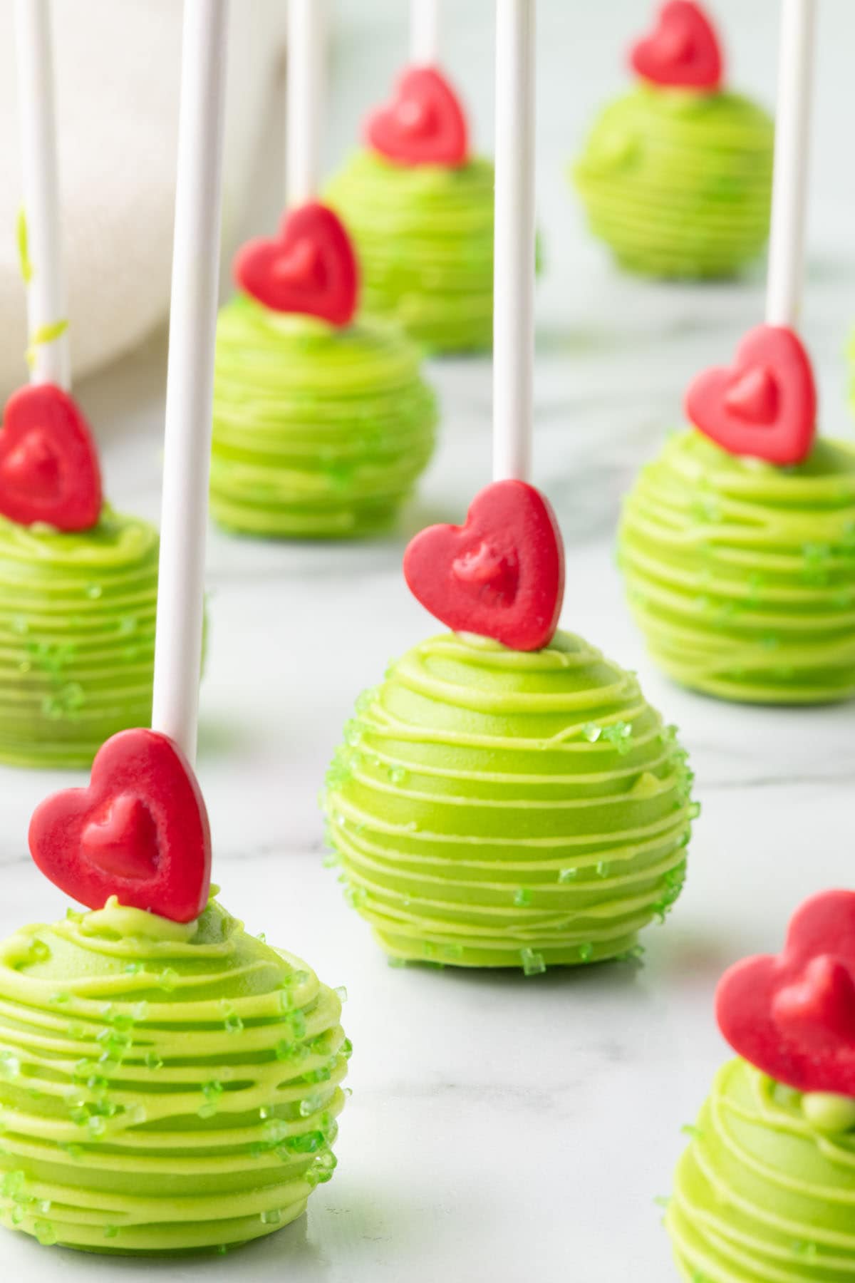 a couple of Grinch Cake Pops on the table with candy heart on top. 