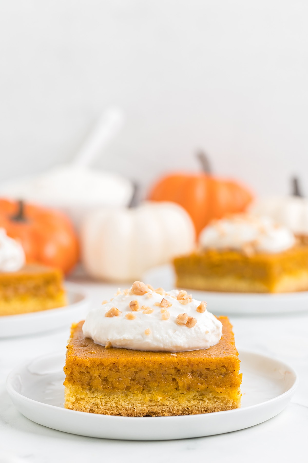 Pumpkin Gooey Butter Cake on a white plate with pumpkin on the background.