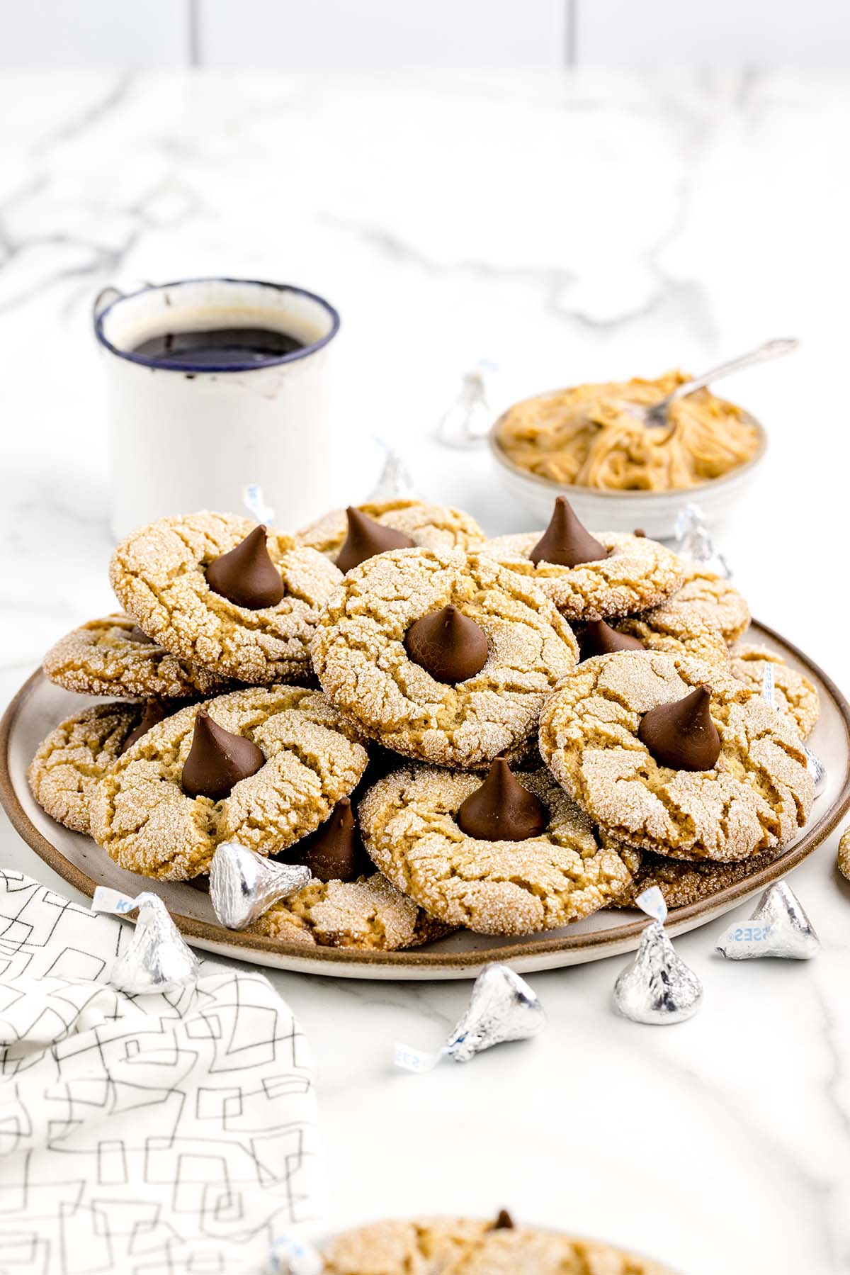 Peanut Butter Blossoms on a large plate with black coffee on top of white table.