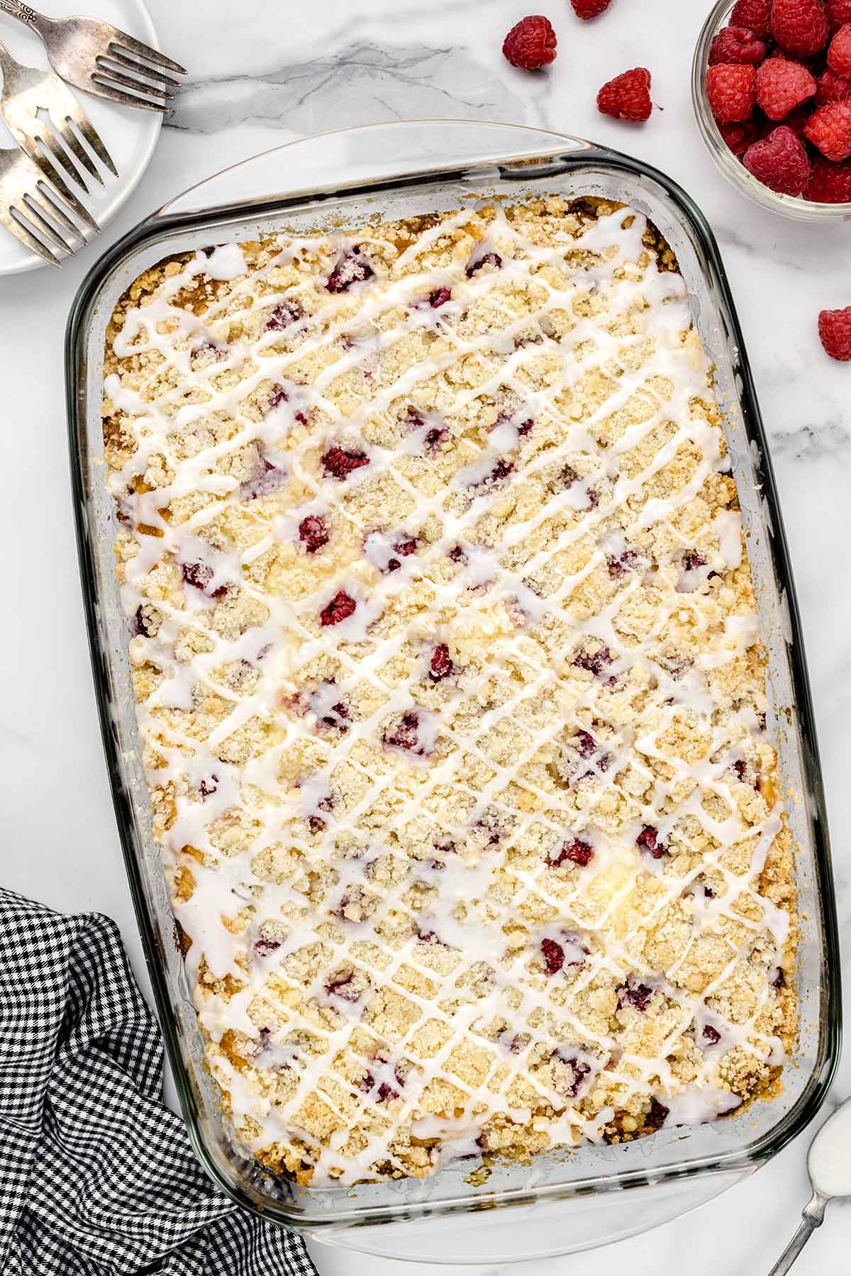 Raspberry Coffee Cake in a baking dish drizzled with glaze on top.