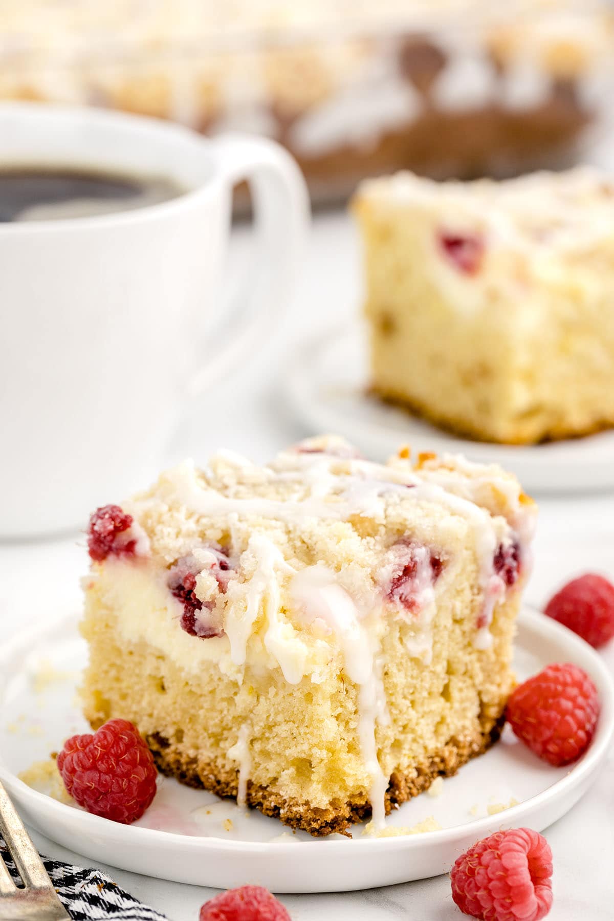 a slice of Raspberry Coffee Cake on a white plate with black coffee on the background.