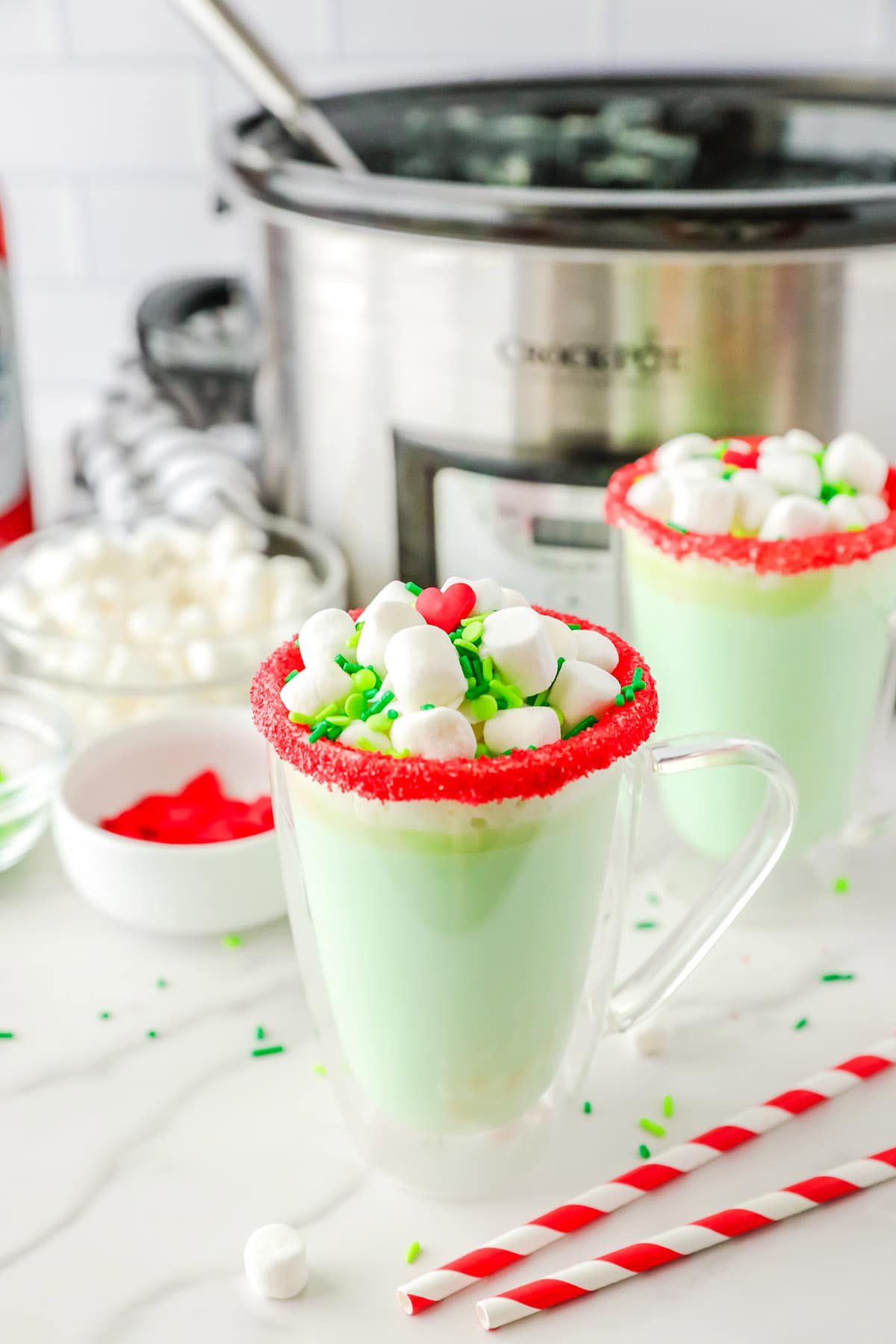 Slow Cooker Grinch Hot Chocolate in a glass with decorated rims and topped with marshmallows.