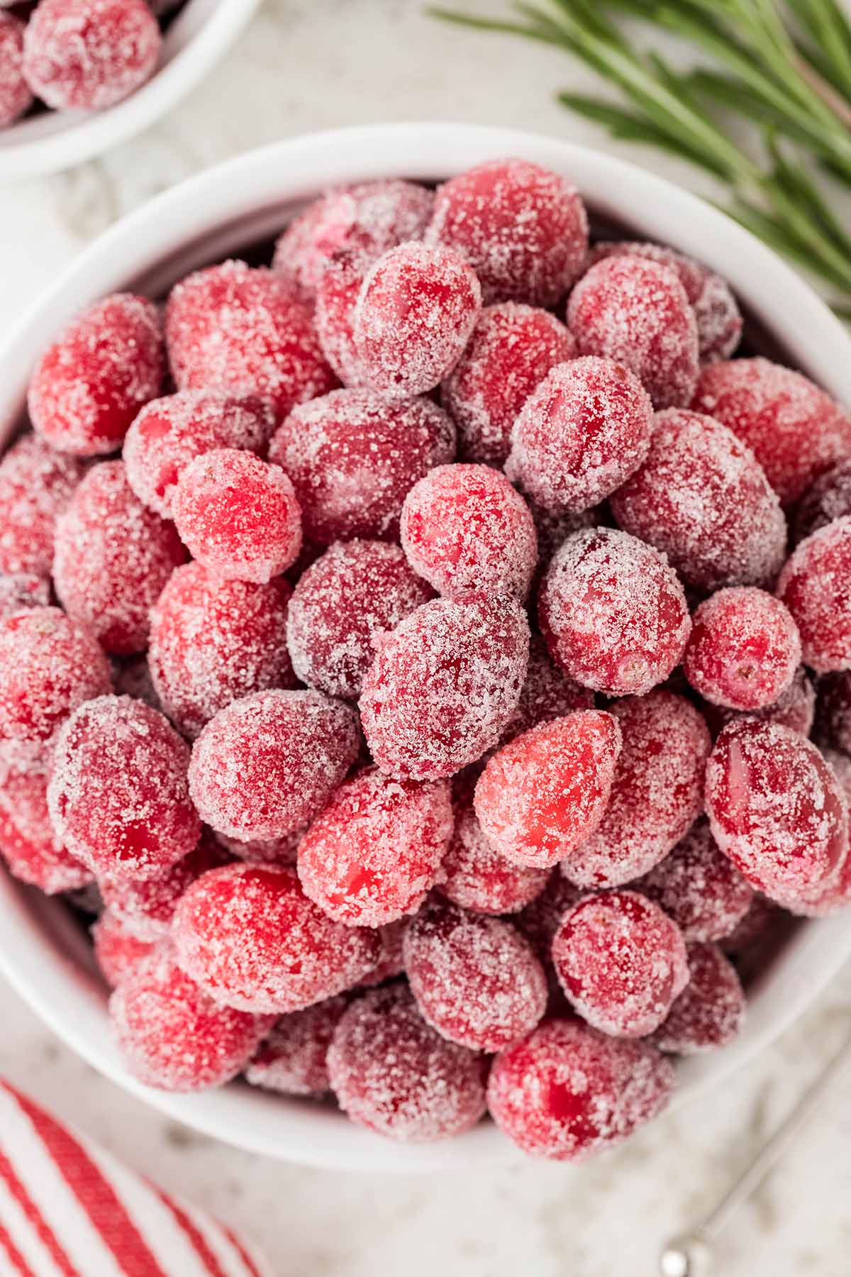 Sugared Cranberries in a white bowl with striped napkin in the background.