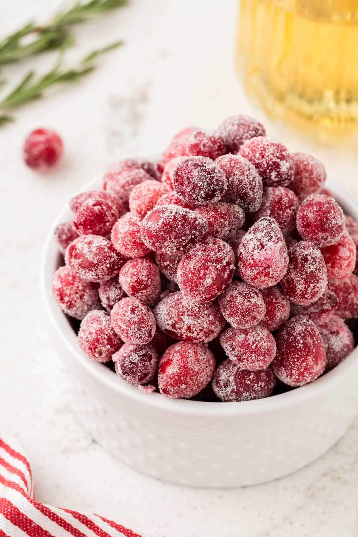 Sugared Cranberries on a white table with a glass of beverage in the background.