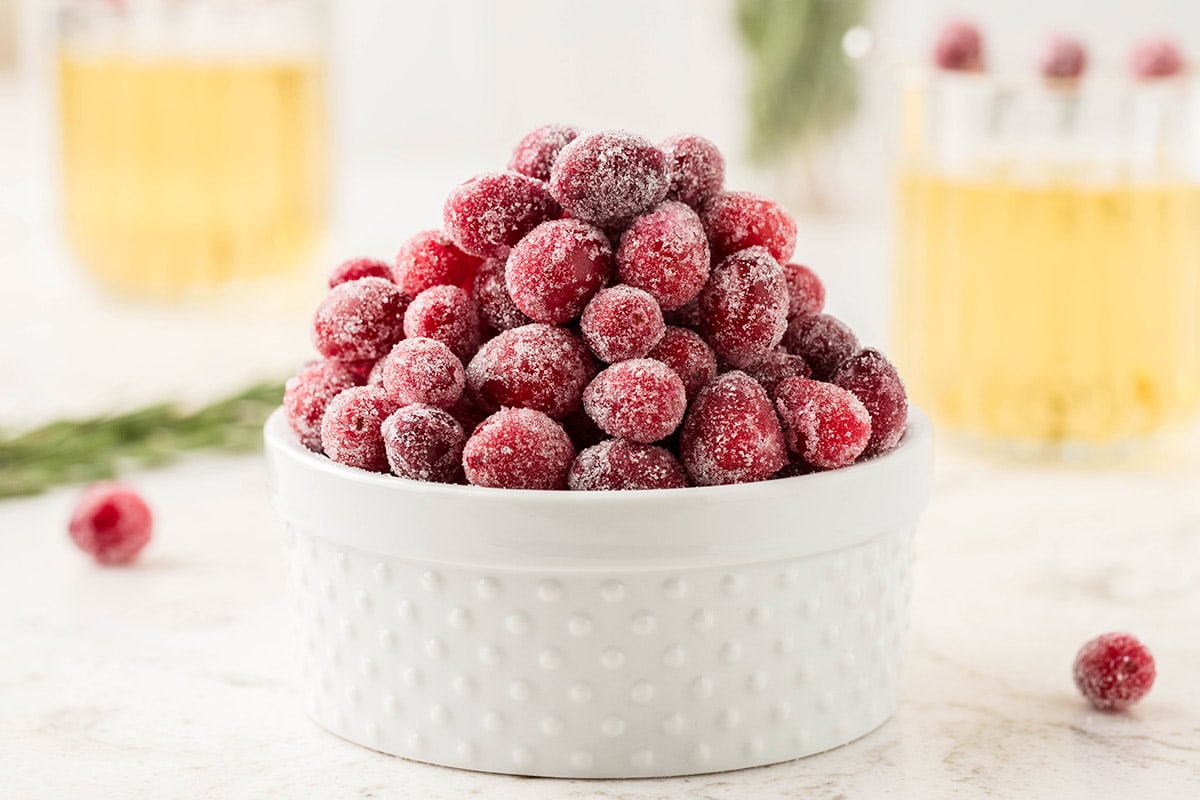 a couple of Sugared Cranberries in a bowl with 2 glasses at the background.