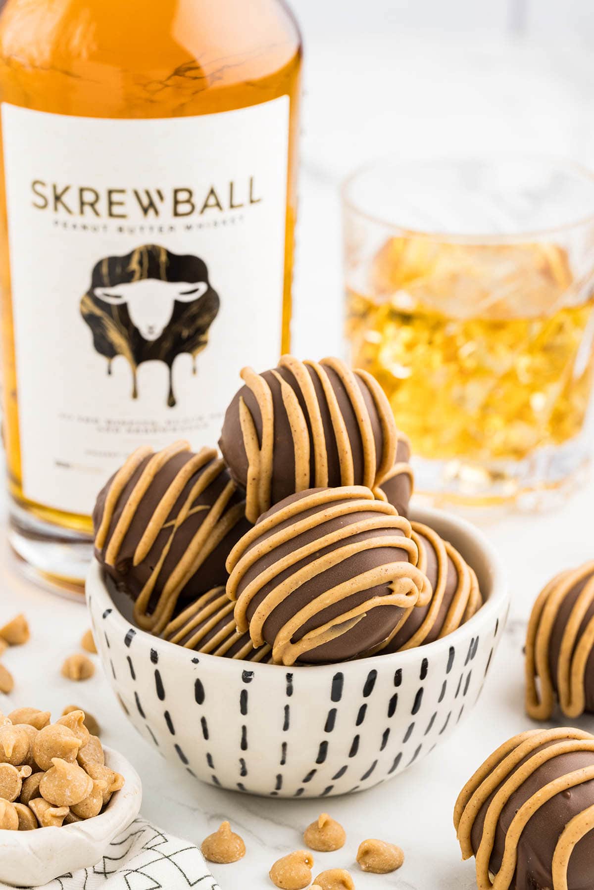 a couple of Whiskey Balls in a bowl with a glass of whiskey and a bottle of skrewball whiskey on the background.
