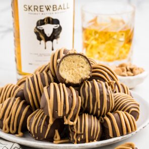 a couple of Whiskey Balls on a plate and bottle of Screwball whiskey on the background.