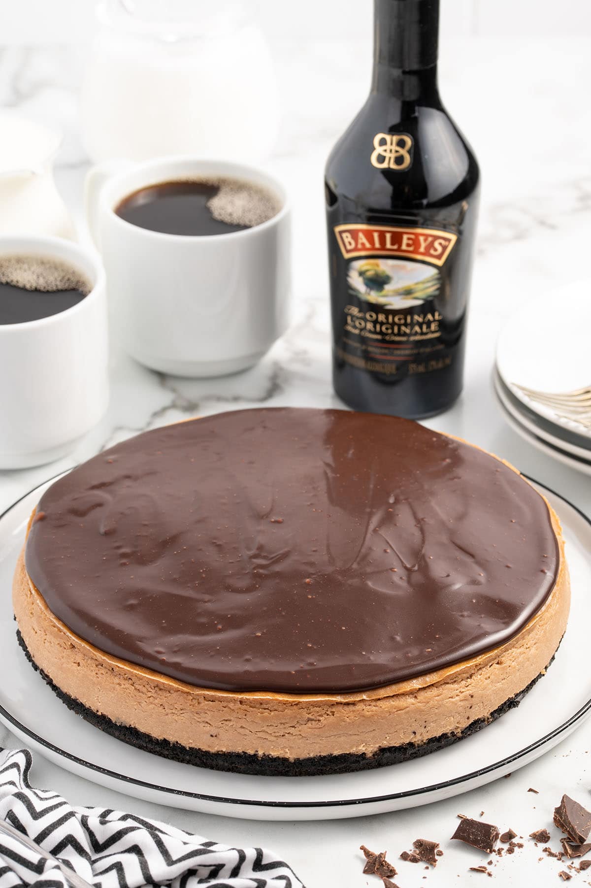 whole Bailey's Cheesecake on a white plate and 2 glasses of black coffee on the background.