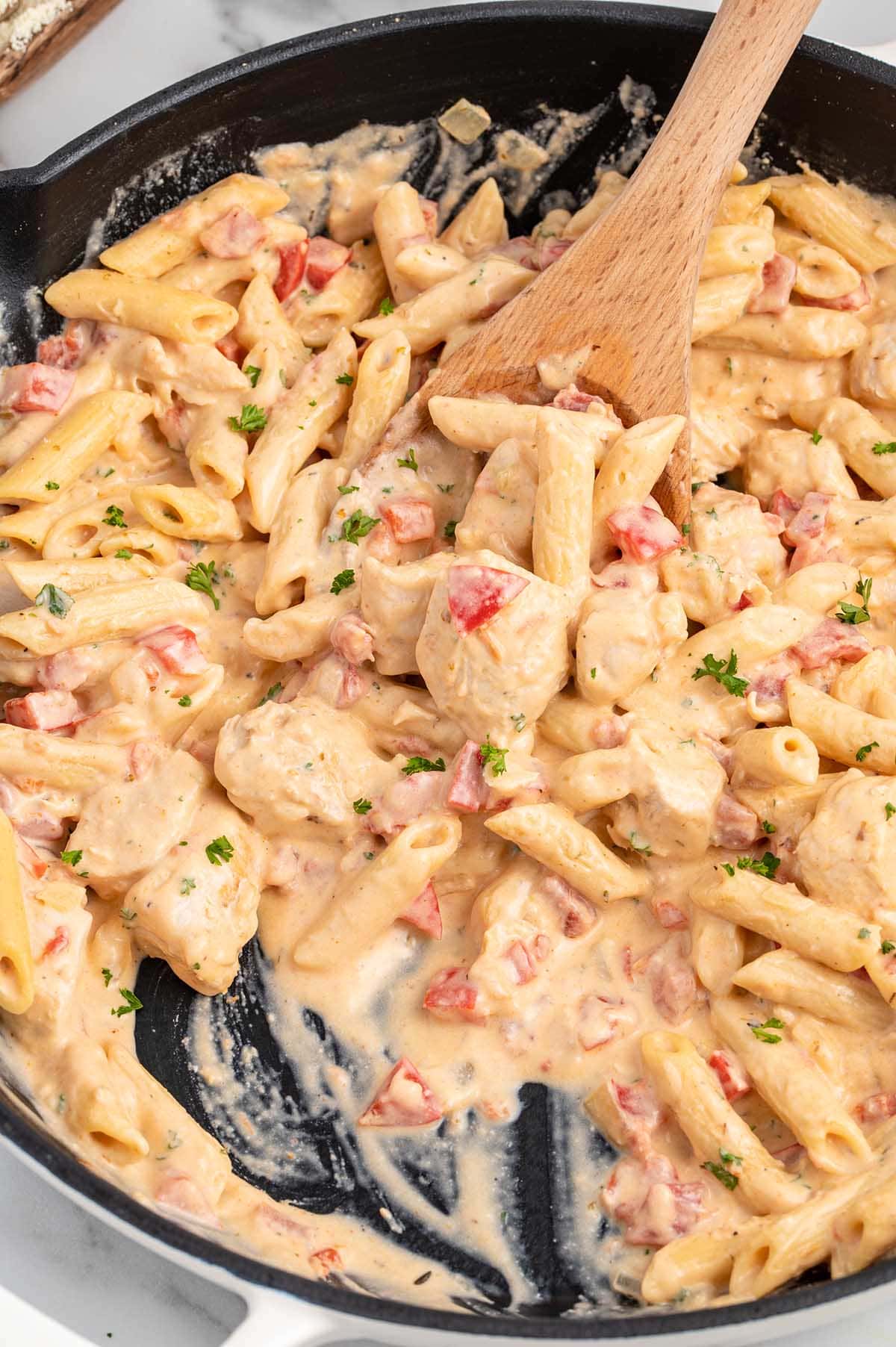 stirring Cajun Chicken Pasta in a skillet with a wooden spoon.