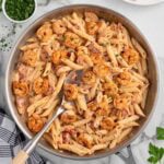 Creamy Cajun shrimp pasta with penne, seasoned shrimp, and diced tomatoes in a skillet, garnished with fresh parsley.