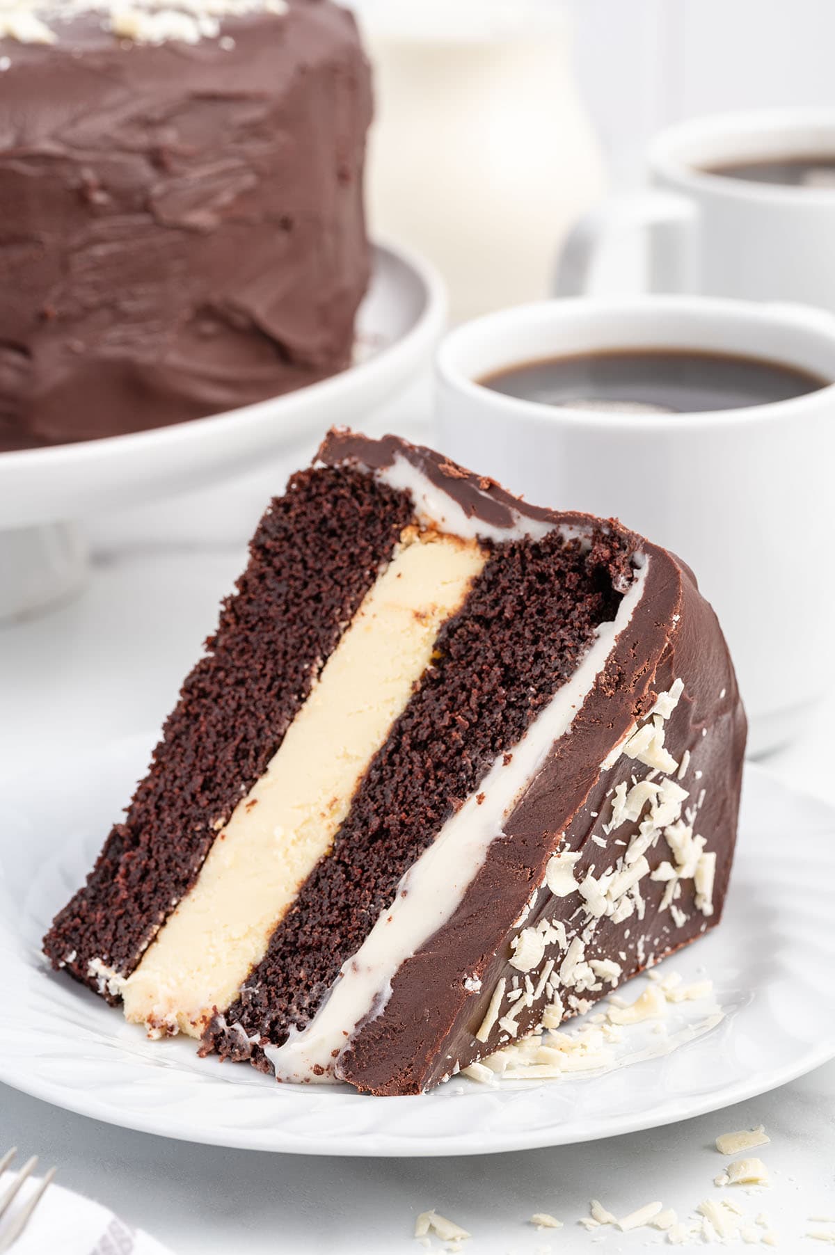 Chocolate Layer Cheesecake with Cream Cheese Filling sliced on plate with a coffee at the back.