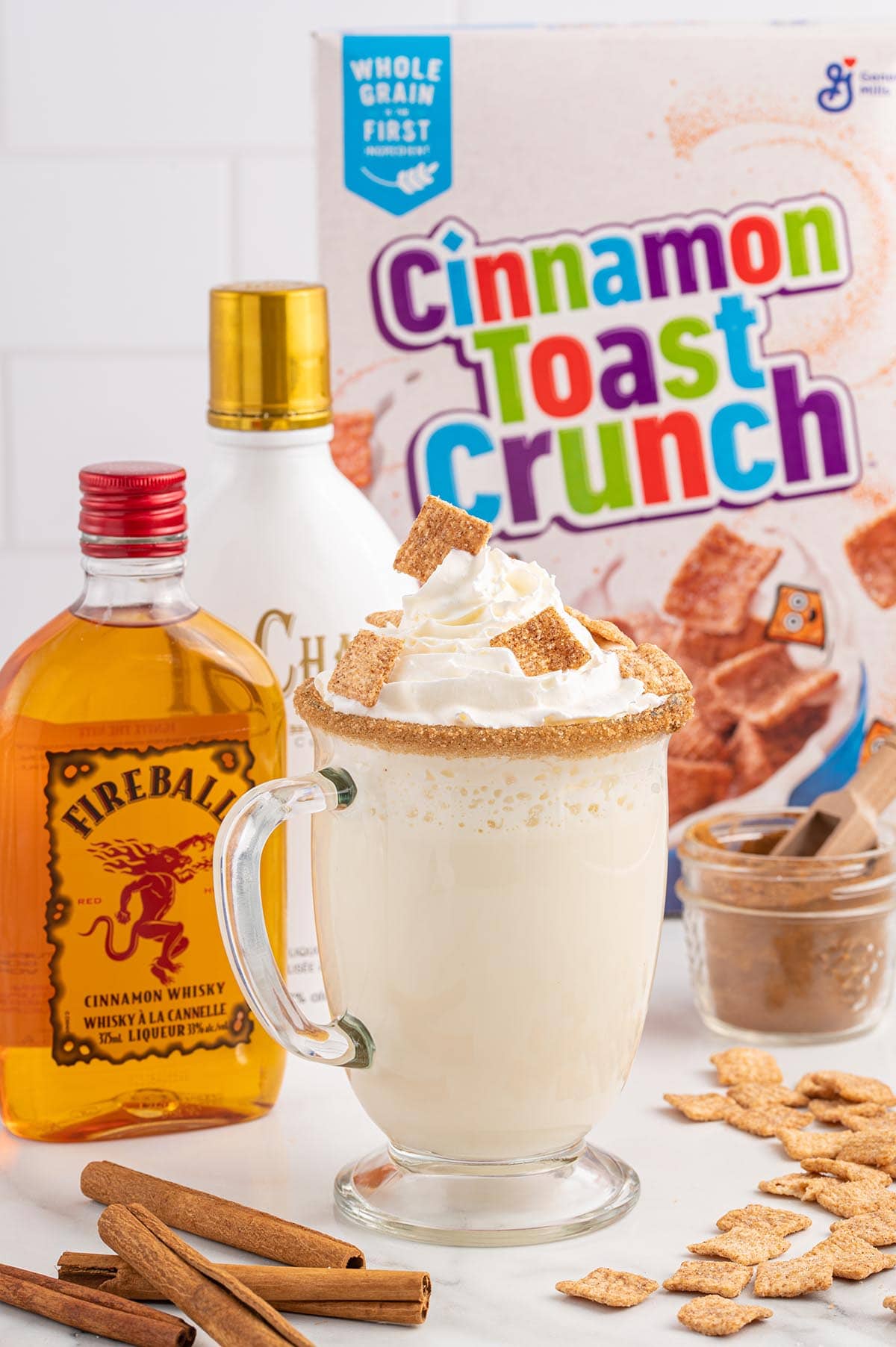 A glass mug of Cinnamon Toast Crunch Cocktail and some cinnamon stick and cinnamon toast crunch cereal scattered on the table.