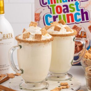 2 glasses mug of Cinnamon Toast Crunch Cocktail with whipped cream and cinnamon toast crunch cereal on top.