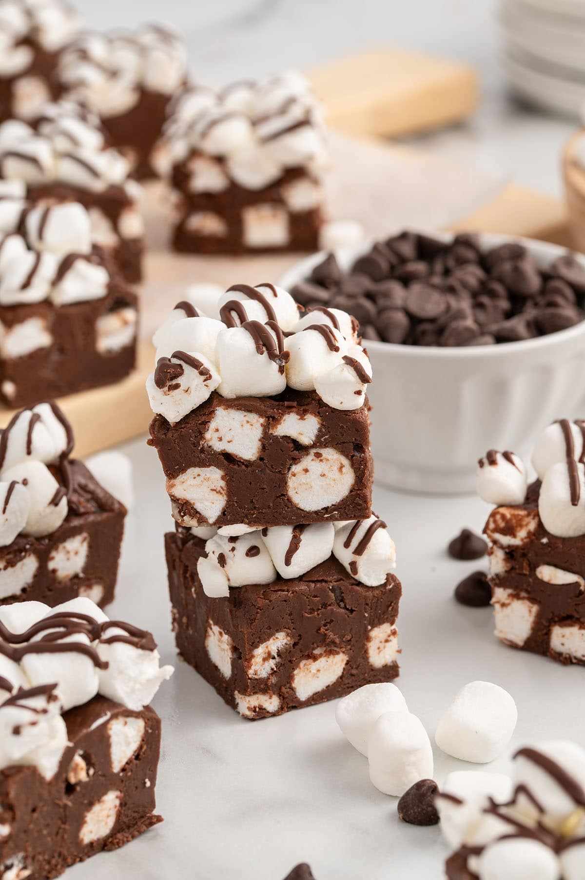 Fudge squares topped with marshmallows and chocolate drizzle arranged with chocolate chips and marshmallows.