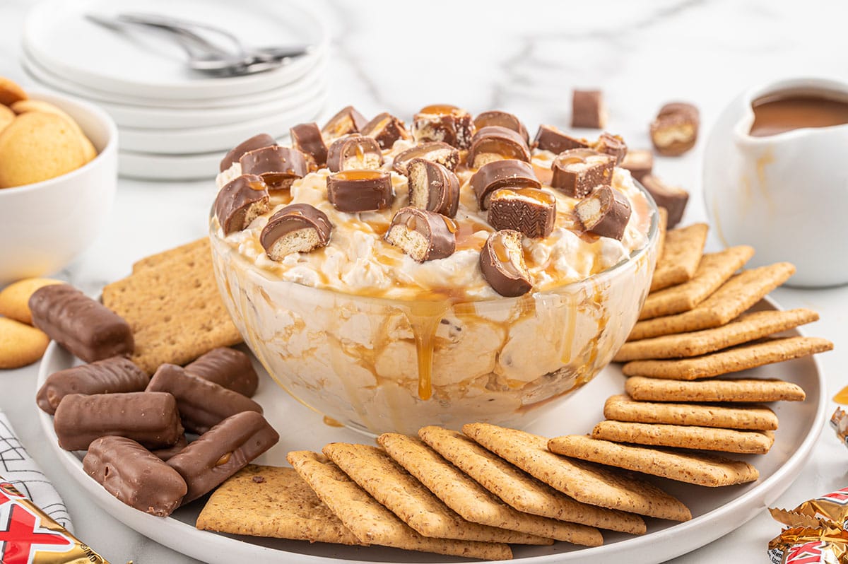 Twix Dip in a bowl with chopped candy bar on top and crackers surrounding the bowl. 