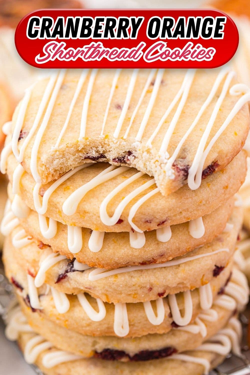 Stacked cranberry orange shortbread cookies with white icing drizzle, top cookie with a bite taken out.