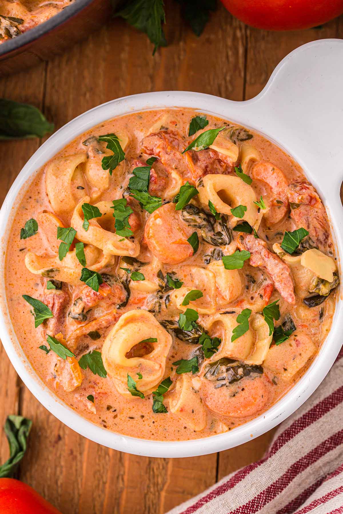 Creamy Tortellini Soup in a white bowl with striped  napkin on the side.