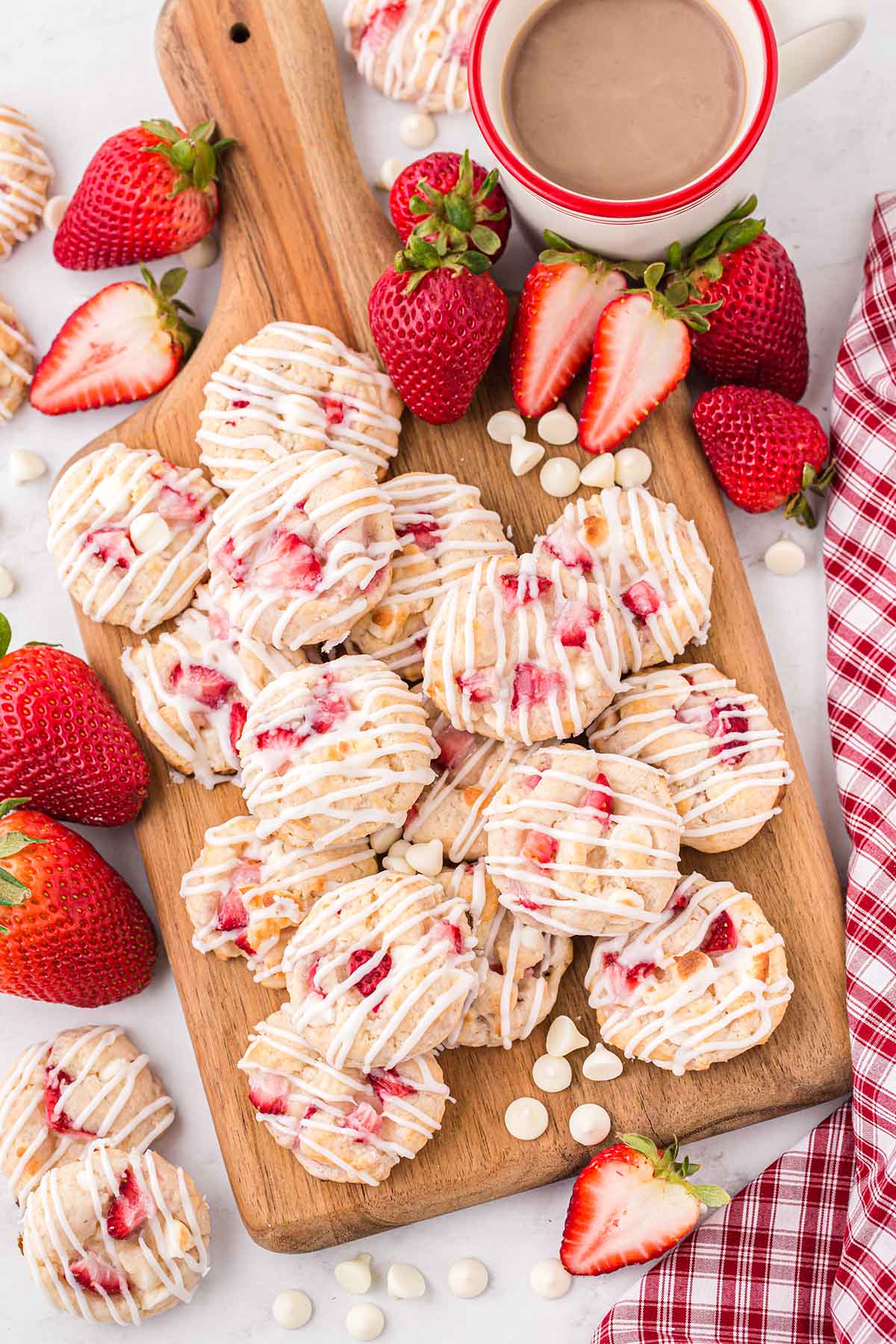 a couple of Strawberry Shortcake Cookies on a wooden board and some strawberries on the table.