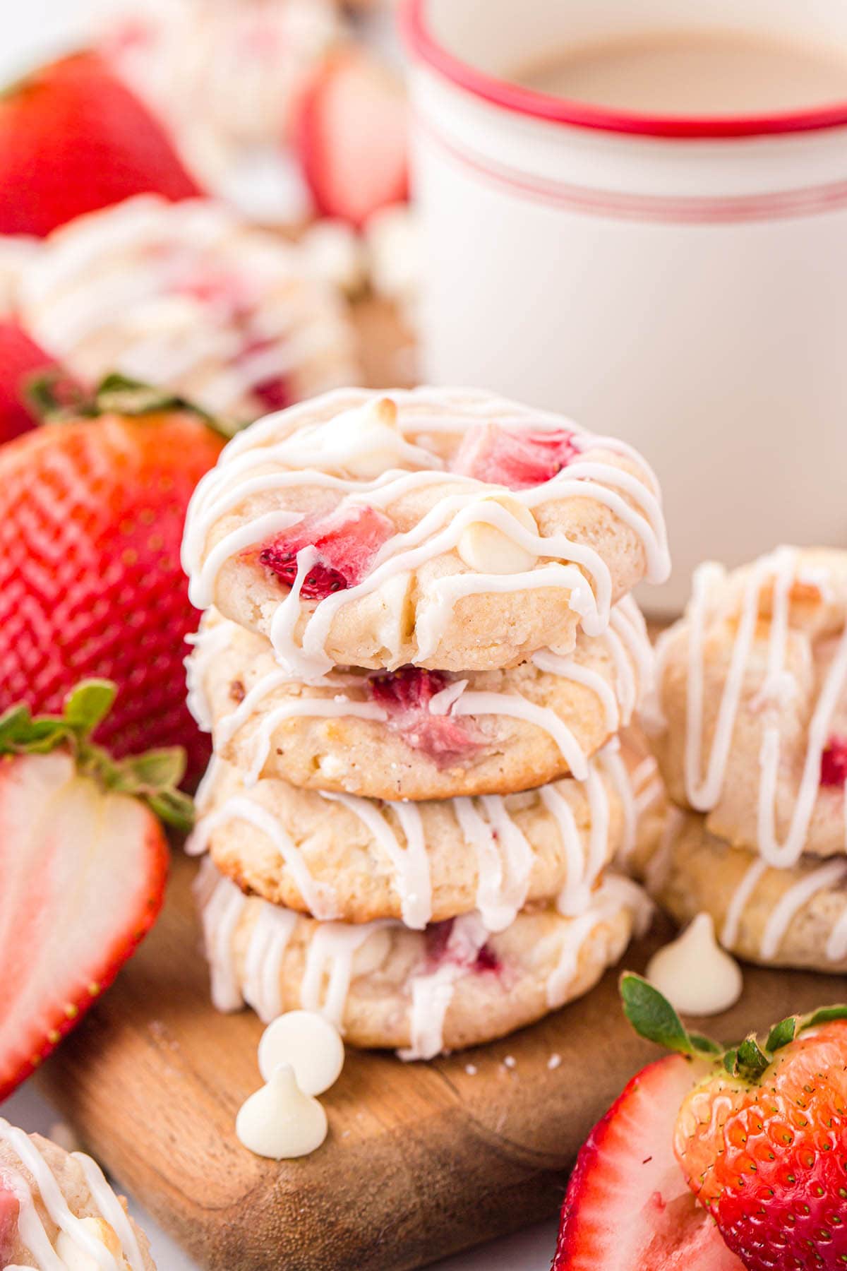 a couple of Strawberry Shortcake Cookies stacked on top of wooden board with a couple of fresh strawberries at the background.
