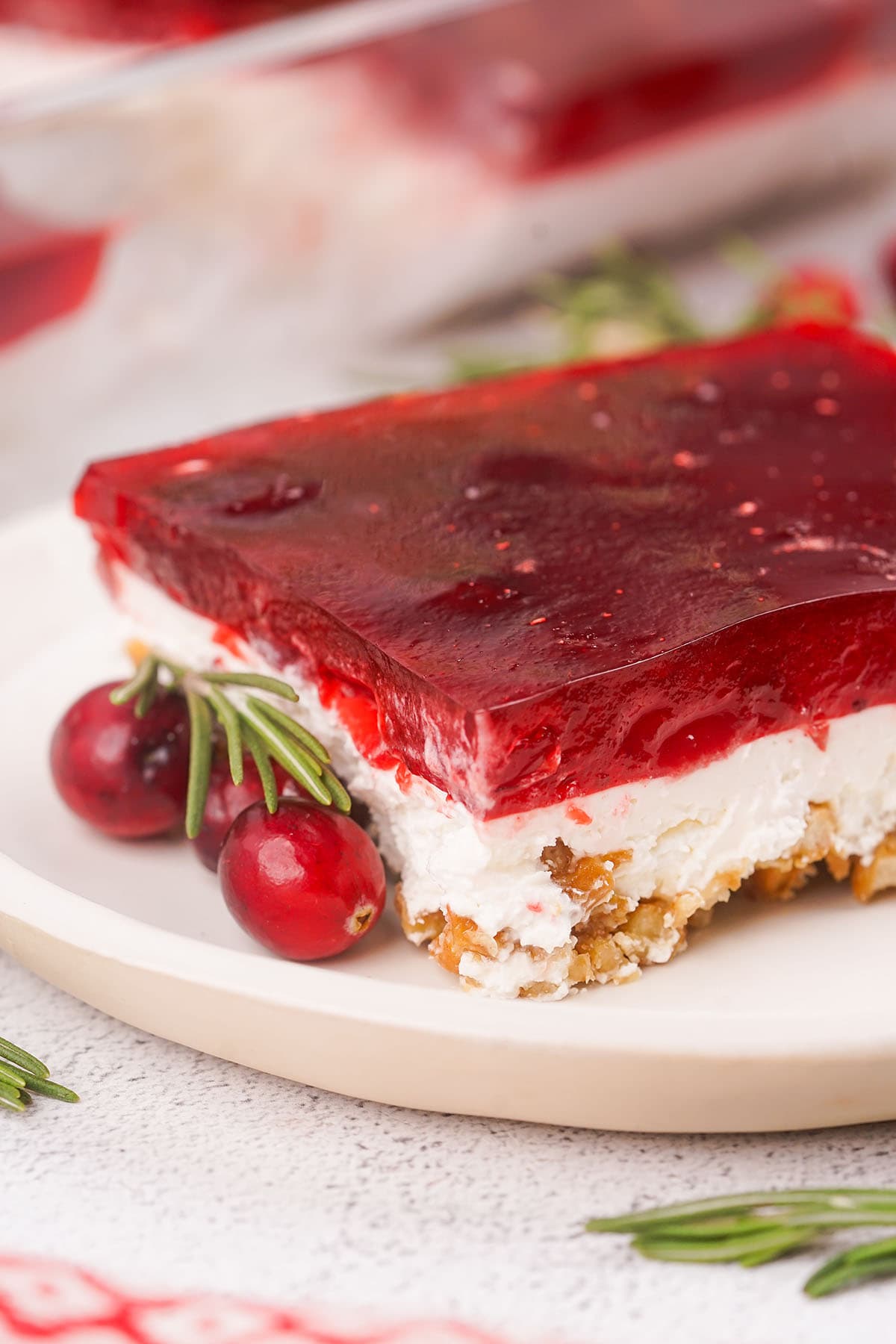 Cranberry Pretzel Salad on a white table with fresh cranberries on the plate.