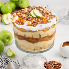 Caramel Apple Trifle in a trifle bowl with apple slices and chopped pecans on top.