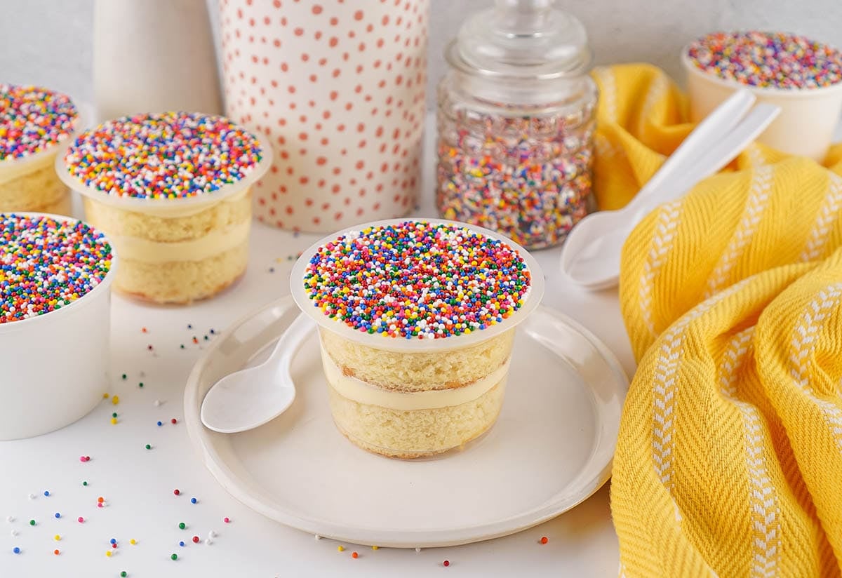 Layered vanilla cake cup topped with colorful rainbow sprinkles.