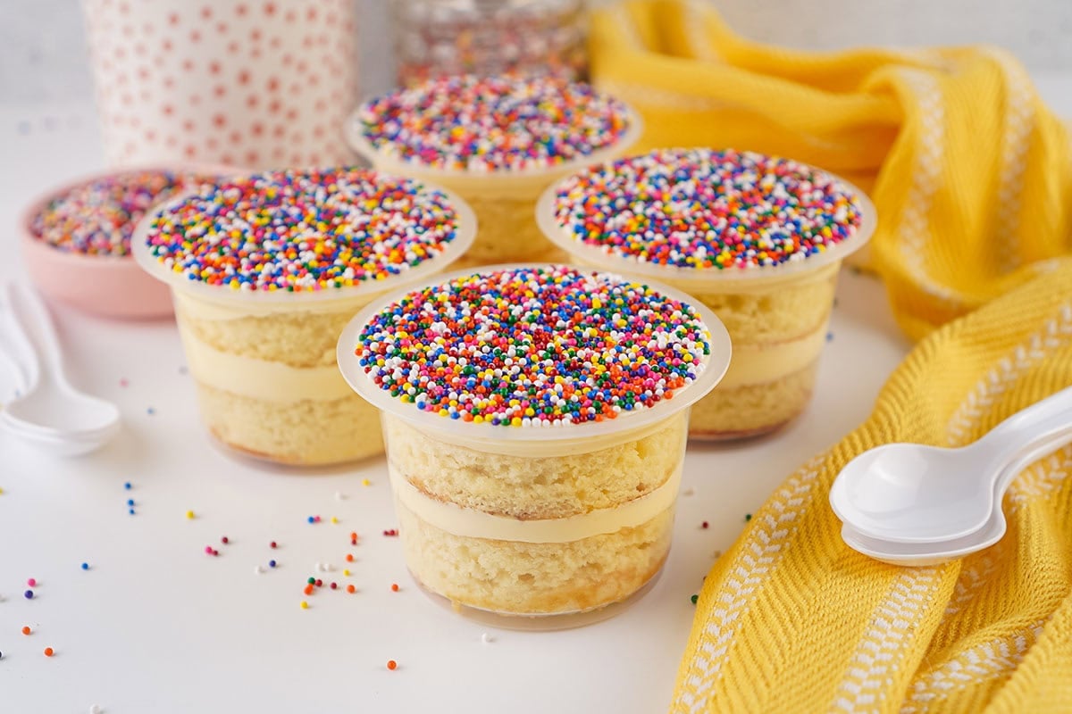 Layered vanilla cake cups topped with rainbow sprinkles.