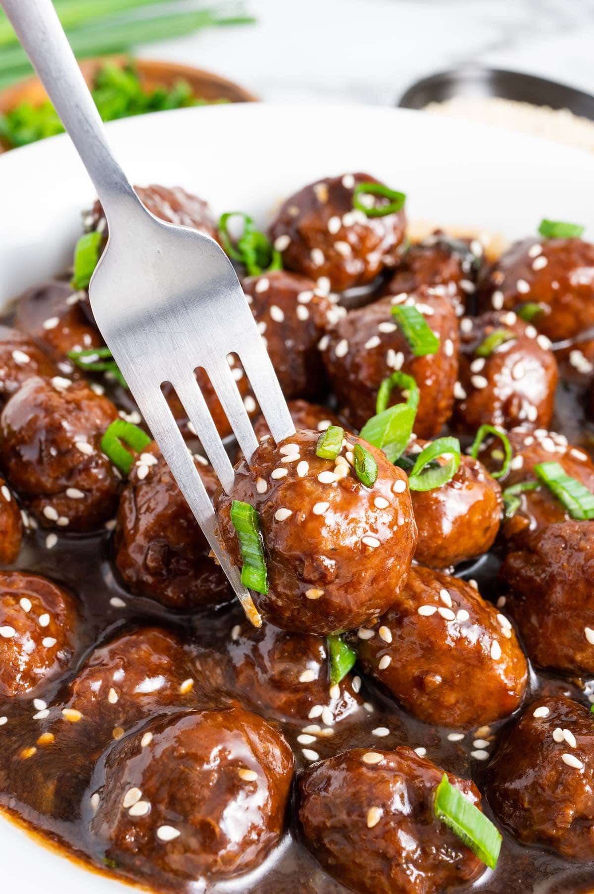 using a fork to eat Teriyaki Meatballs from a large white bowl.