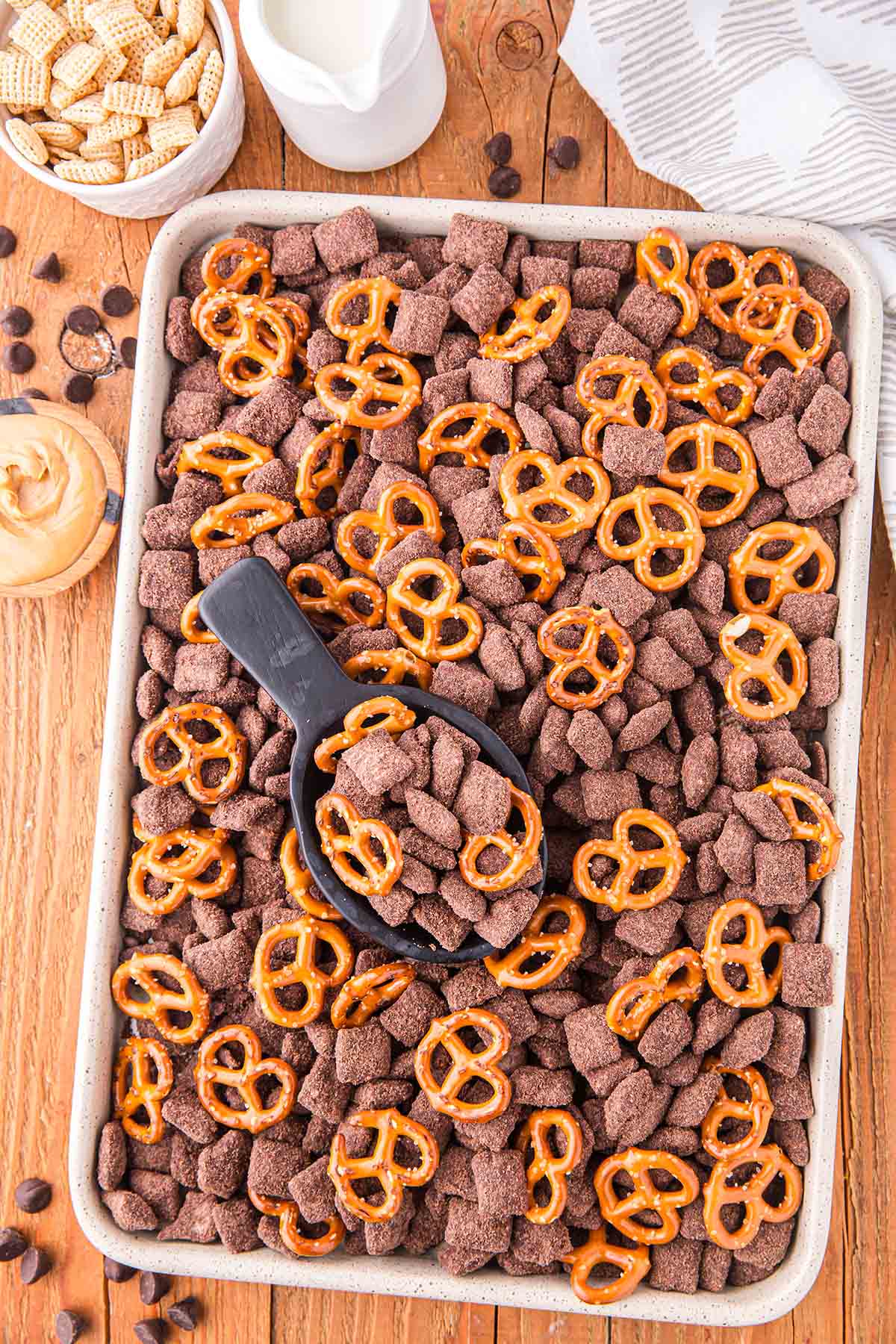 Brownie Batter Puppy Chow in a large baking tray with some pretzels on top.