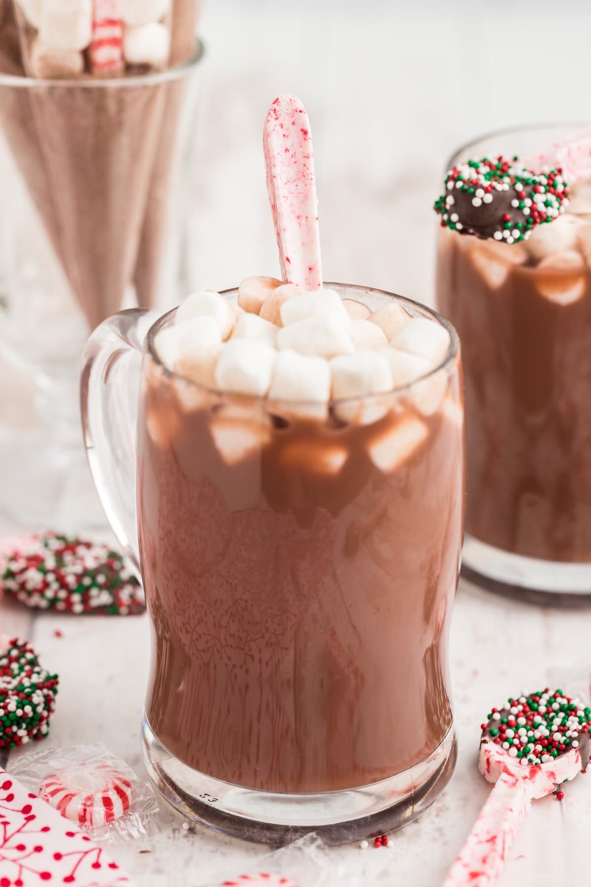 peppermint candy spoon dipped in a glass of hot chocolate with marshmallows on top.