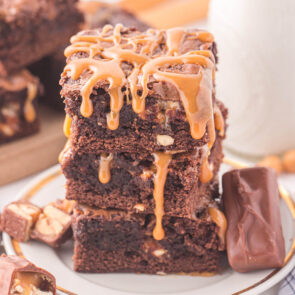 Snickers Brownie stacked on a plate drizzled with caramel sauce.