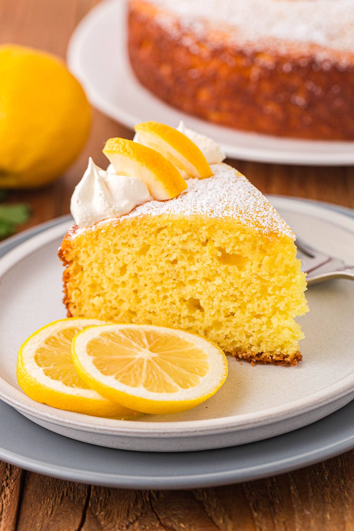 a slice of Lemon Ricotta Cake with 2 slices of lemon on a plate.