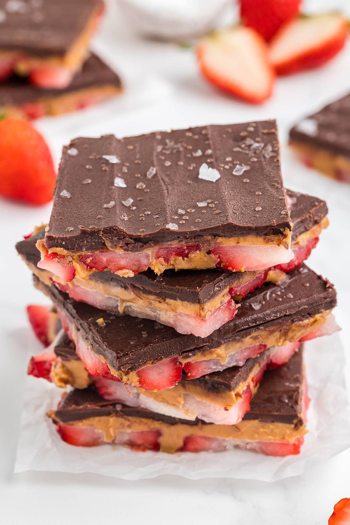 a couple of Strawberry Peanut Butter Bark on the table with strawberries on the background.