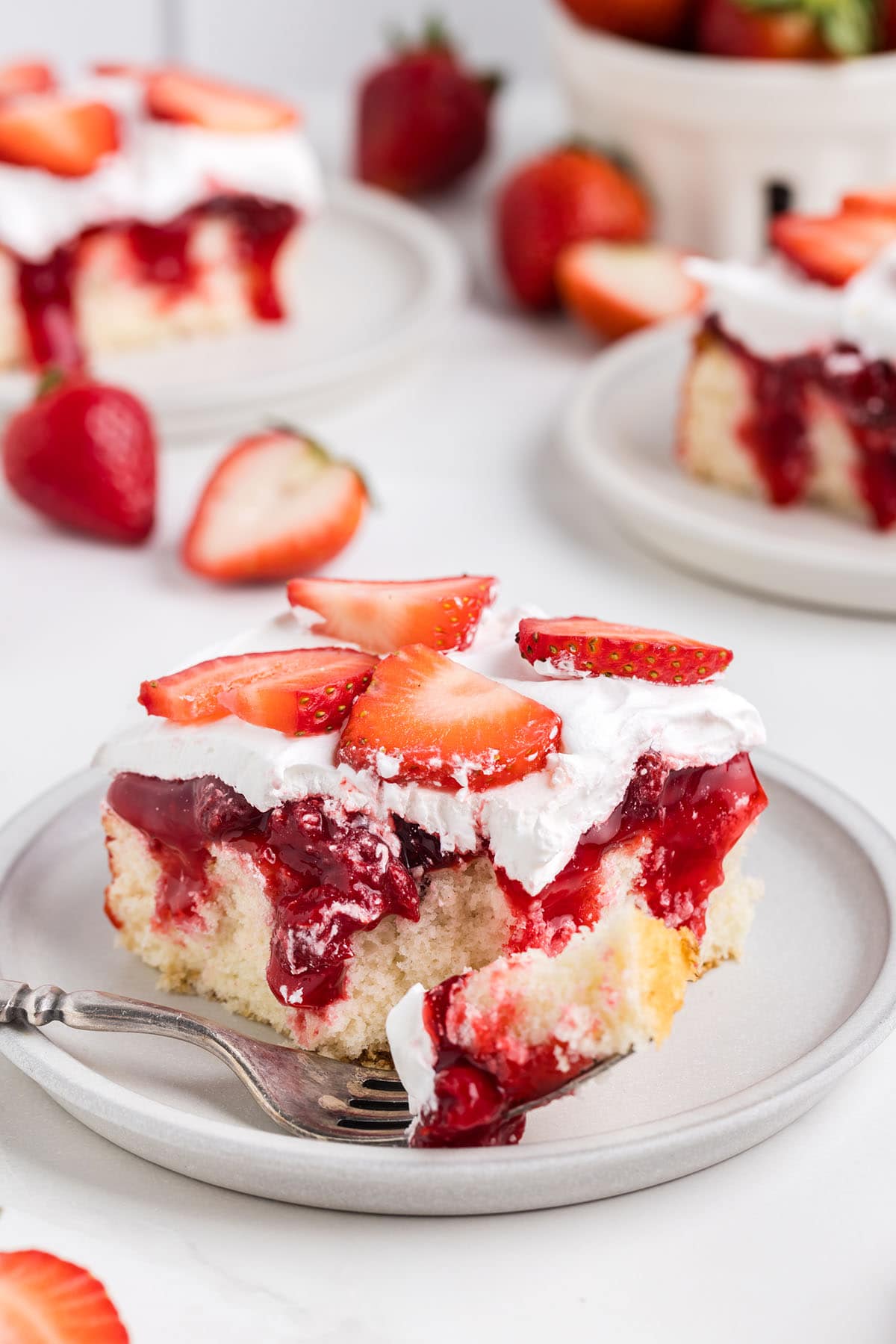 eating a slice of Strawberry Shortcake Poke Cake using a fork on a plate.