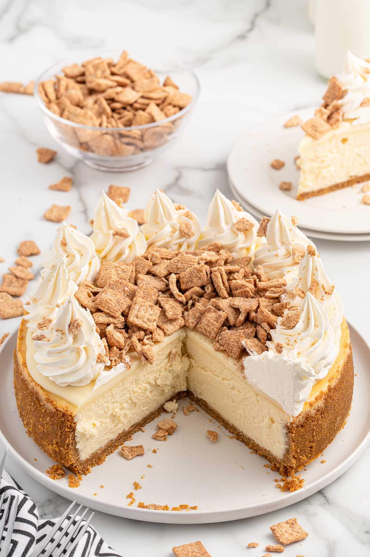 cinnamon toast crunch cheesecake on a plate with a slice of cheesecake on another plate.