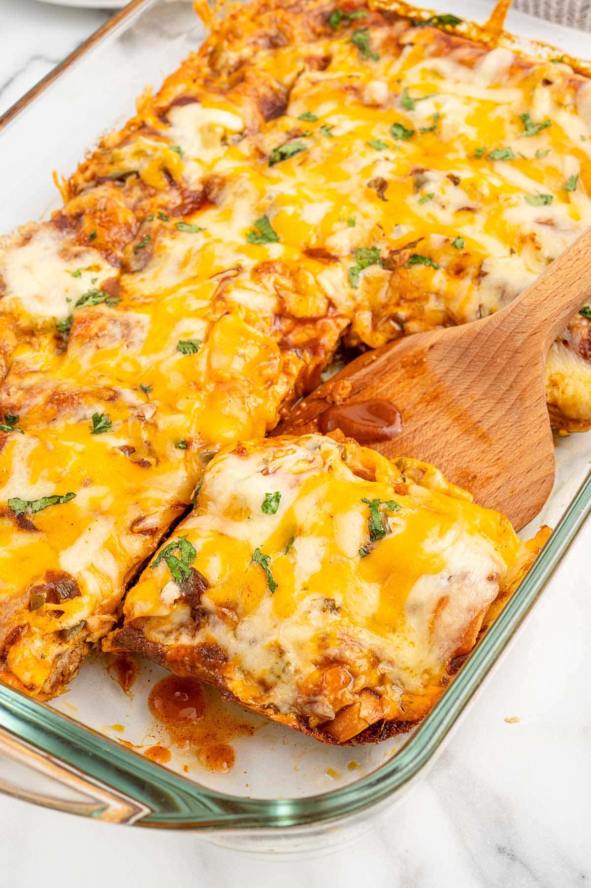 taking a square piece of lazy enchiladas from casserole dish using wooden spoon.