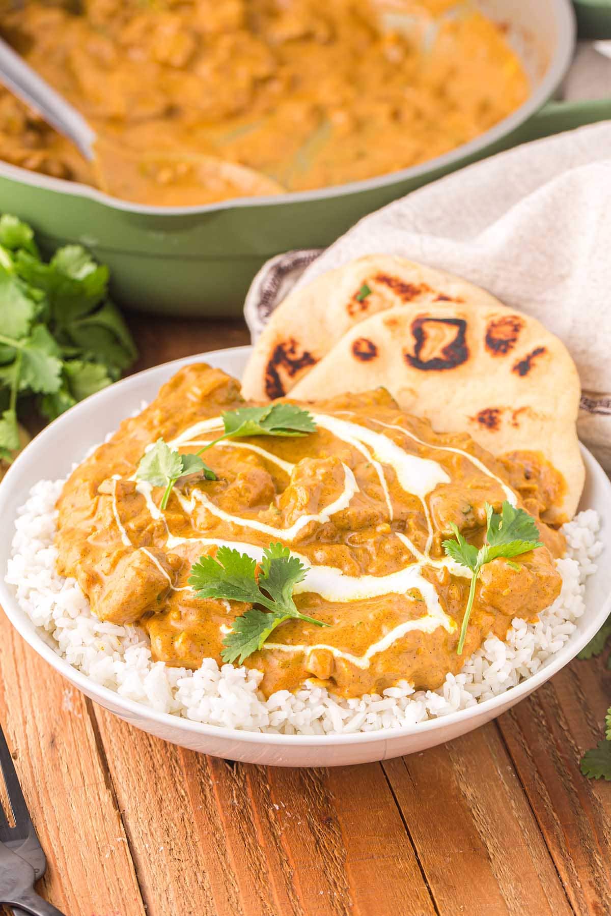 Indian Butter Chicken over a bowl of rice with a couple of naan bread.