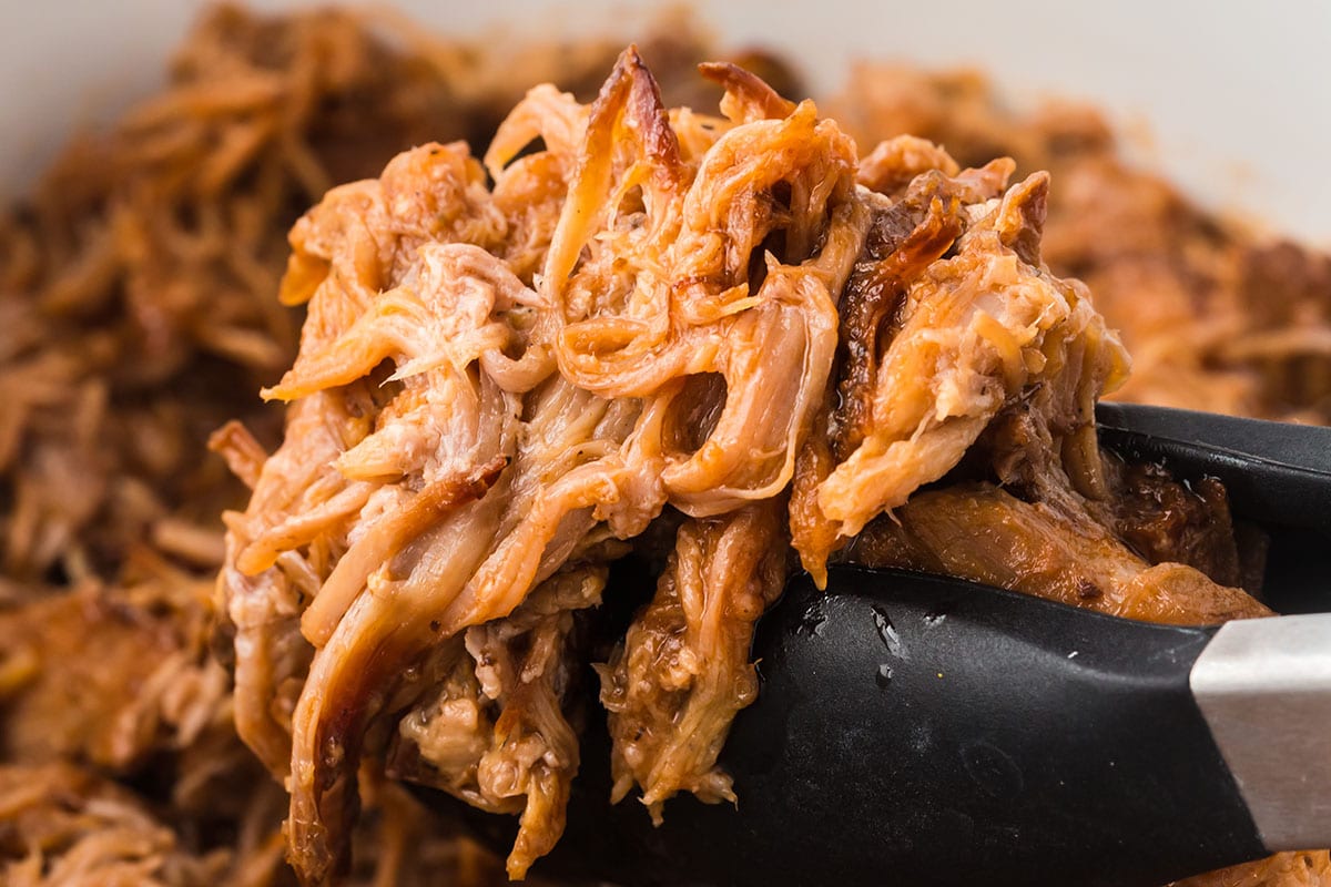 using tong to take Coca-Cola Pulled Pork from crockpot.