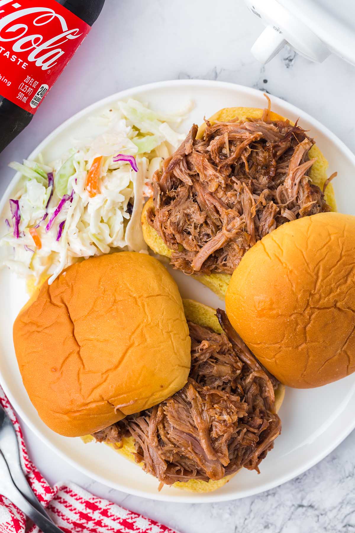 Crockpot Coca-Cola Pulled Pork inside buns on a plate with coleslaw.