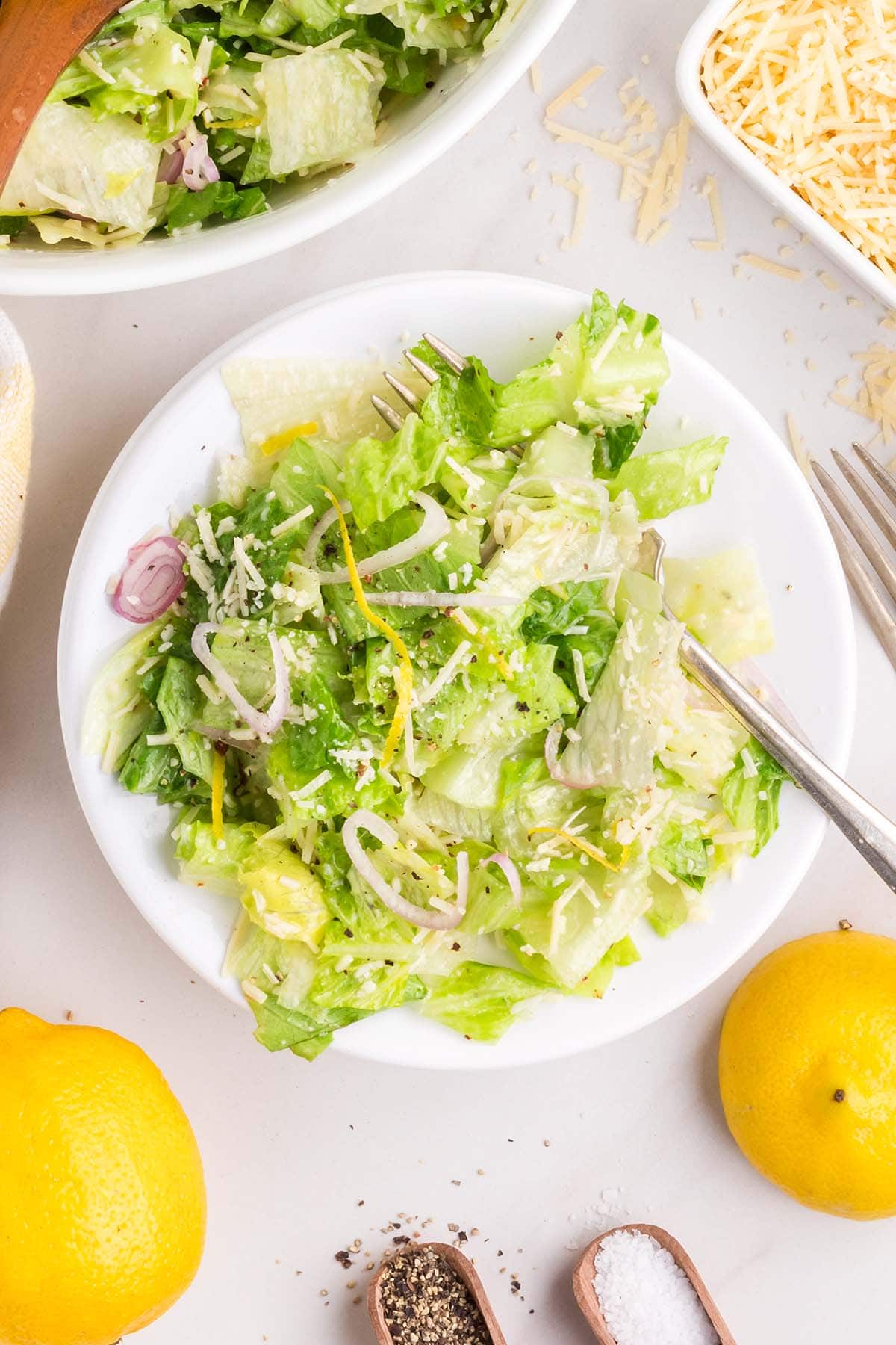 lemon parmesan salad on a plate with a fork on the side and a couple of lemons on the background.
