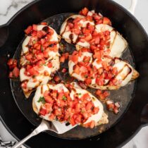 Bruschetta chicken with mozzarella, tomatoes, basil, and balsamic glaze in a skillet.