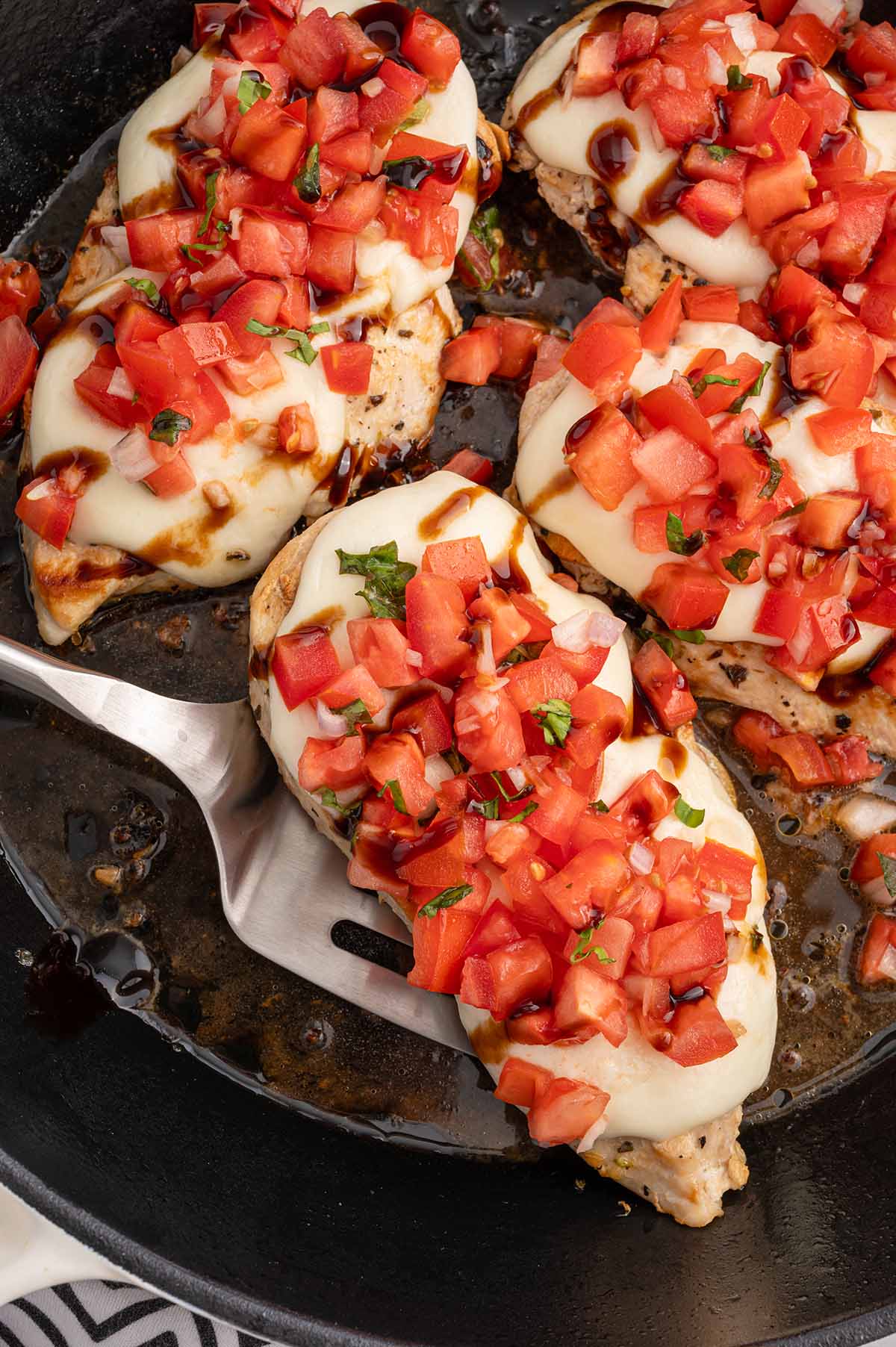 Close-up of bruschetta chicken topped with mozzarella, diced tomatoes, basil, and balsamic glaze in a skillet.