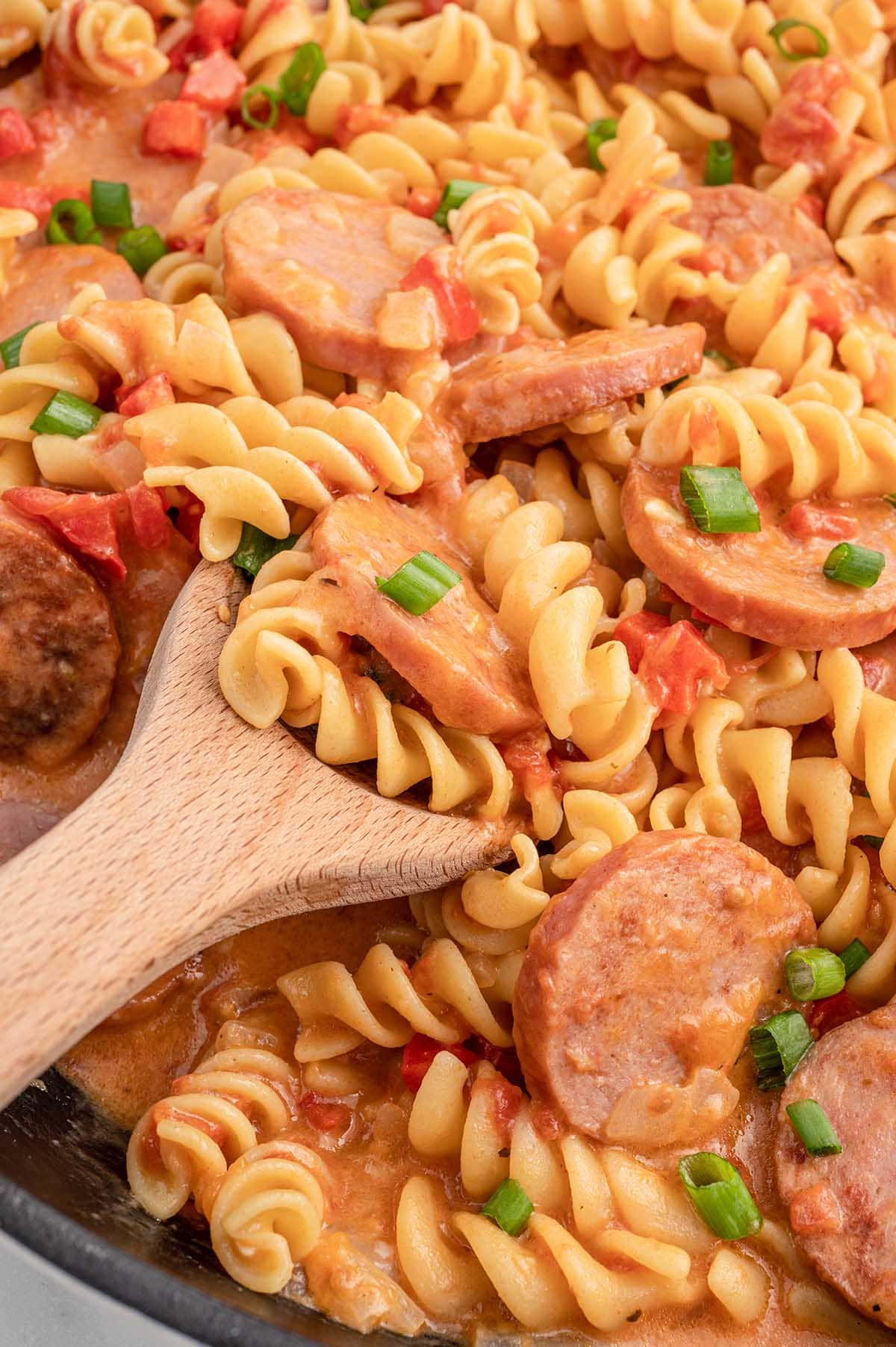 take a big scoop of Italian Sausage Pasta using a wooden spoon.