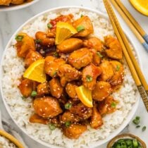orange chicken served over a bowl of rice.
