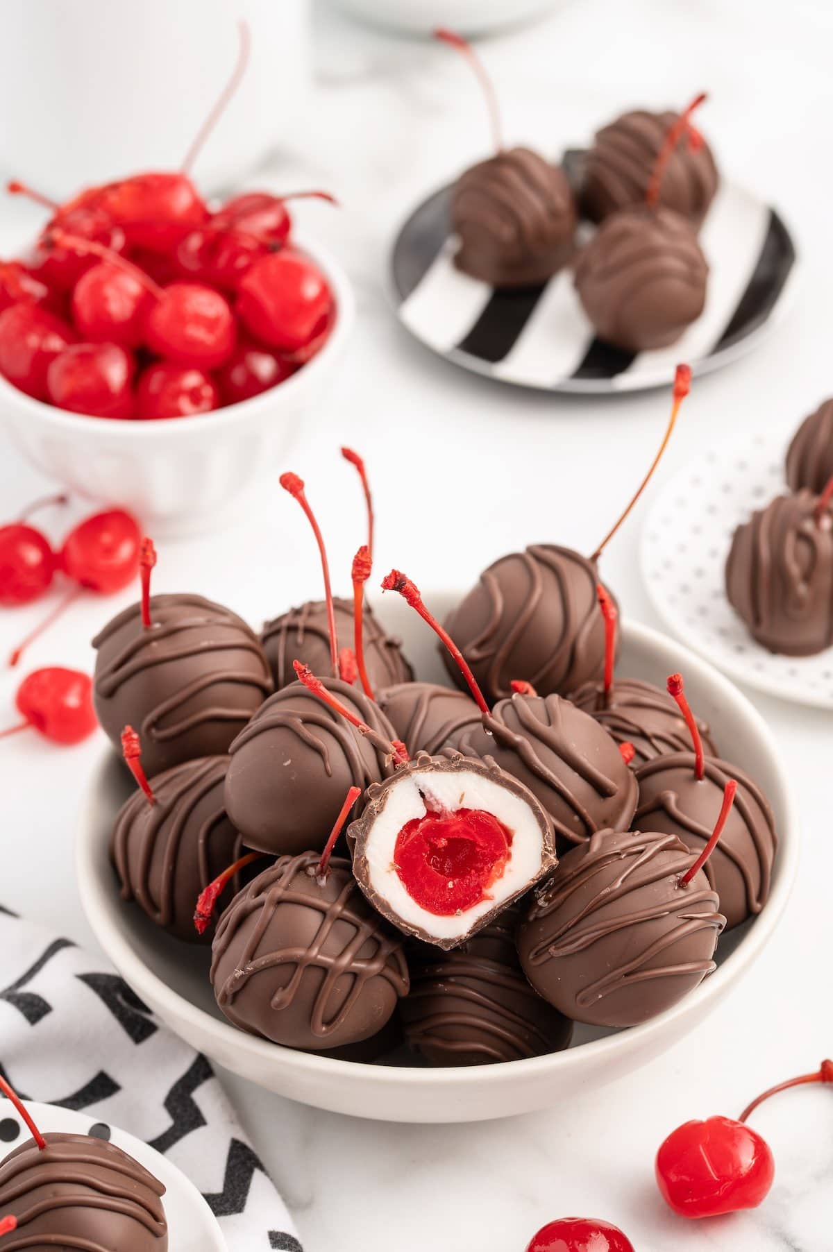 a couple of Chocolate Covered Cherries in a bowl with a bowl full of maraschino cherries on the background.