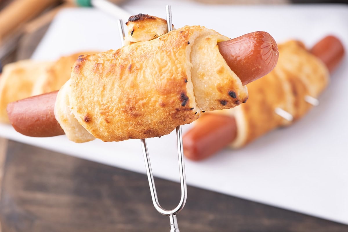 cooked Campfire Crescent Roll Hot Dogs on a skewer.