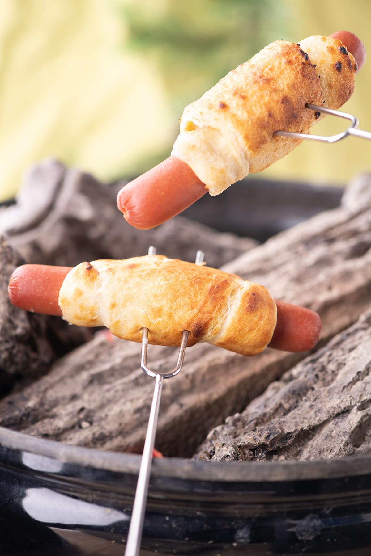 cooking 2 hot dogs wrapped with dough using a skewers.