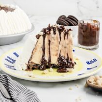 a slice of Hula Pie on the plate and extra chocolate sauce at the back and oreo cookies.